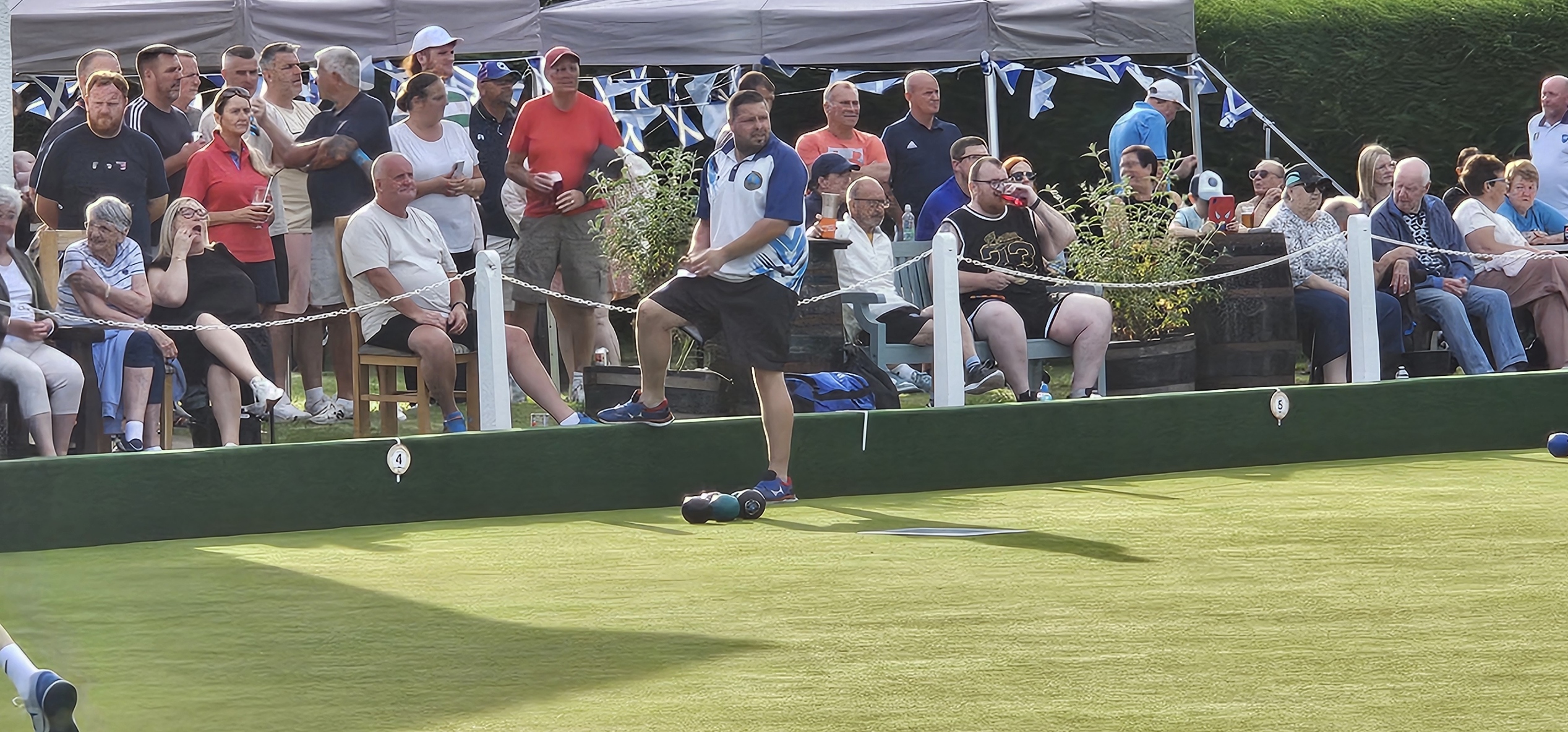 Gary Malcomson stepping up to the mat during the fiercely contested Gents Pairs match, surrounded by watching supporters